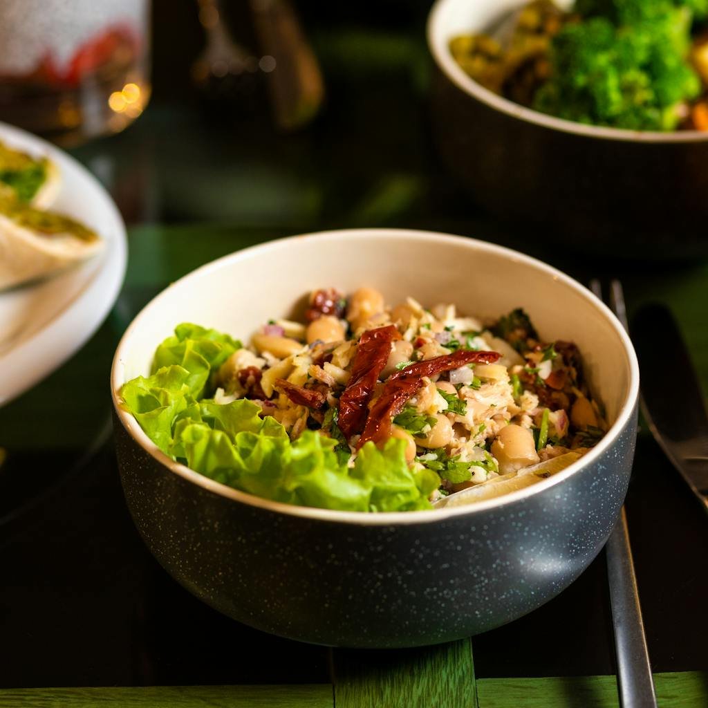 Delicious mixed bean salad topped with sun-dried tomatoes served in a ceramic bowl, perfect for a healthy lunch.