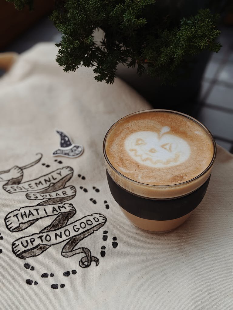 A festive Halloween latte featuring a pumpkin face foam art, perfect for autumn vibes.