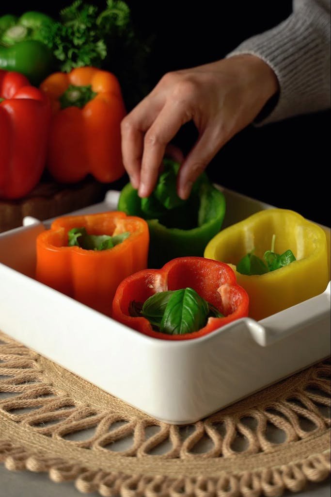 A hand placing basil in colorful bell peppers for a healthy meal.